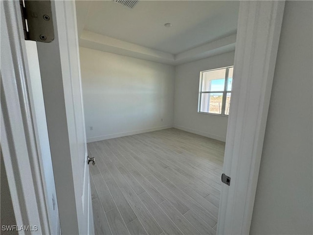 unfurnished room featuring a tray ceiling and light hardwood / wood-style flooring