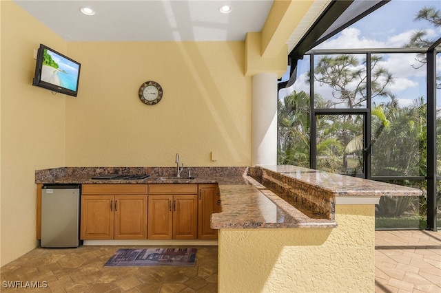 kitchen with stone counters, sink, expansive windows, kitchen peninsula, and refrigerator