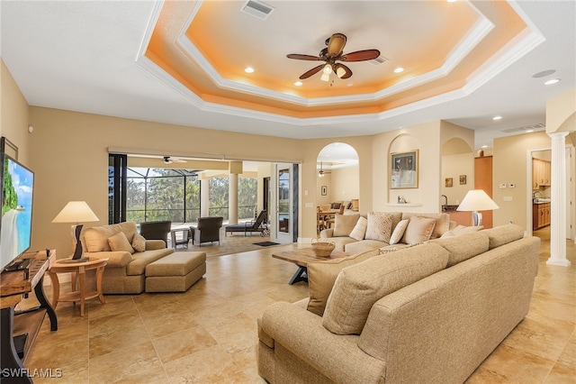 living room with ceiling fan, a raised ceiling, crown molding, and decorative columns