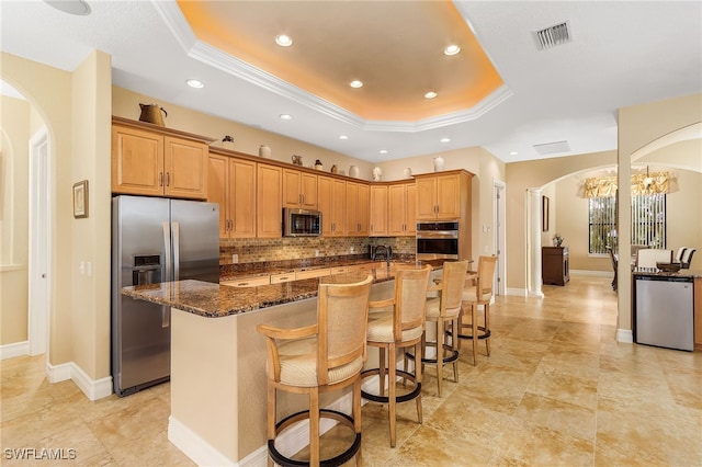 kitchen featuring a notable chandelier, backsplash, a large island with sink, a kitchen bar, and appliances with stainless steel finishes