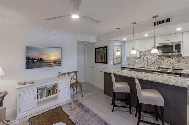 kitchen featuring white cabinets, hanging light fixtures, appliances with stainless steel finishes, and light hardwood / wood-style flooring