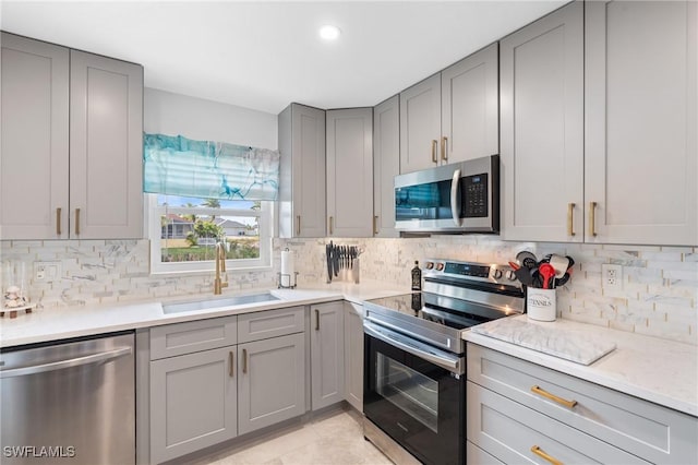 kitchen featuring gray cabinetry, light stone countertops, sink, tasteful backsplash, and appliances with stainless steel finishes