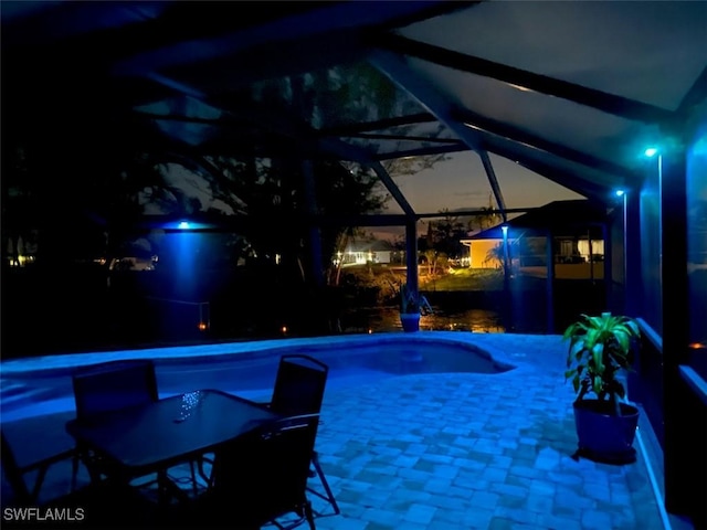 pool at night featuring a patio area and a lanai