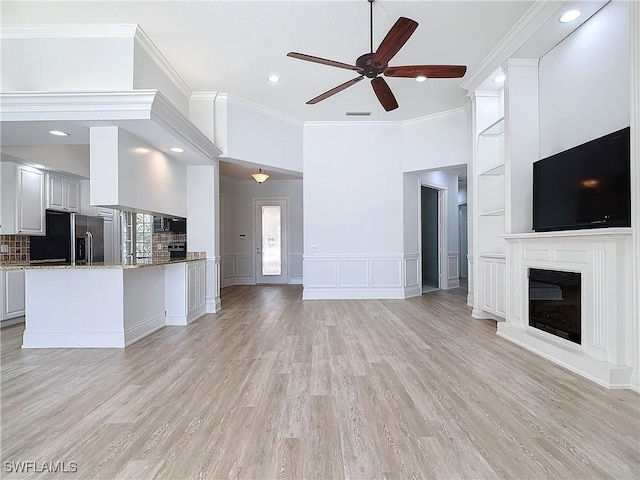 unfurnished living room featuring crown molding, built in features, ceiling fan, and light hardwood / wood-style floors