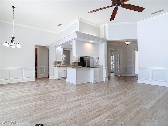 unfurnished living room featuring crown molding, ceiling fan with notable chandelier, and light hardwood / wood-style flooring