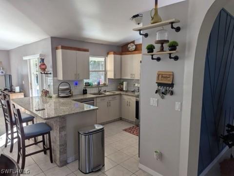 kitchen featuring kitchen peninsula, a kitchen bar, sink, light tile patterned floors, and stone countertops