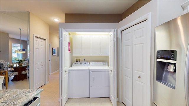 clothes washing area featuring cabinets, light tile patterned floors, and washing machine and dryer