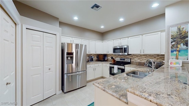 kitchen with light stone countertops, sink, kitchen peninsula, white cabinets, and appliances with stainless steel finishes