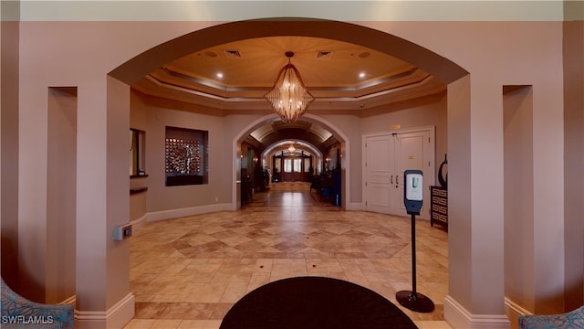 hallway featuring a tray ceiling, ornamental molding, and an inviting chandelier