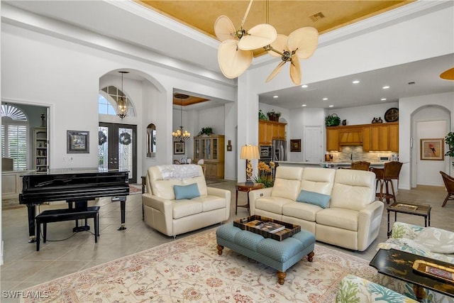 tiled living room featuring ceiling fan with notable chandelier, crown molding, a high ceiling, and a tray ceiling