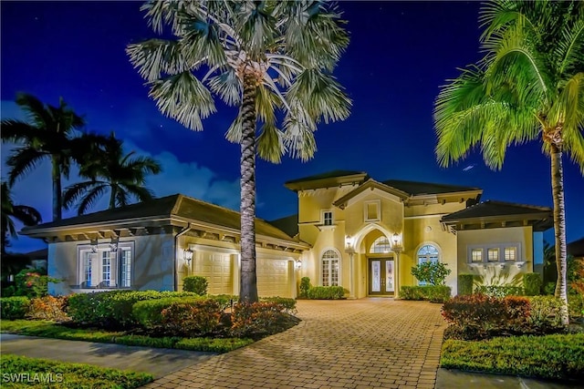 front of house at twilight featuring a garage, french doors, decorative driveway, and stucco siding