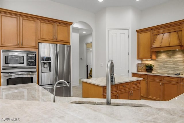 kitchen featuring arched walkways, light stone counters, appliances with stainless steel finishes, a sink, and backsplash