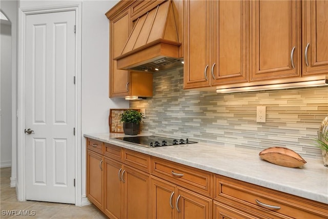 kitchen with light tile patterned floors, brown cabinetry, custom exhaust hood, black electric cooktop, and light countertops