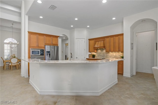 kitchen with stainless steel appliances, light stone countertops, a kitchen island with sink, and backsplash