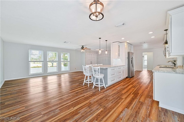 kitchen featuring sink, stainless steel refrigerator with ice dispenser, pendant lighting, wood-type flooring, and white cabinets