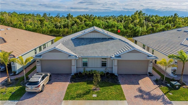 view of front of house featuring a garage, decorative driveway, a tiled roof, and a view of trees