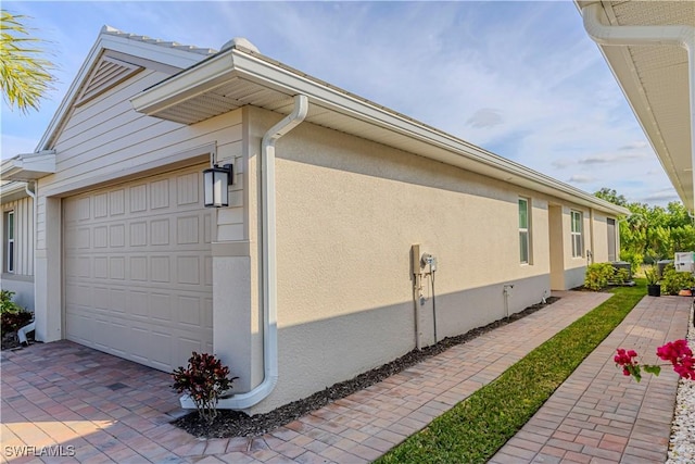 view of property exterior featuring an attached garage, decorative driveway, and stucco siding