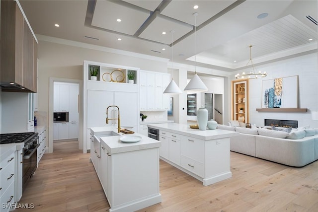 kitchen featuring a large fireplace, decorative light fixtures, a center island with sink, high end stainless steel range, and white cabinetry