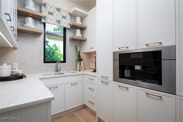 kitchen featuring white cabinets, backsplash, stainless steel oven, and sink