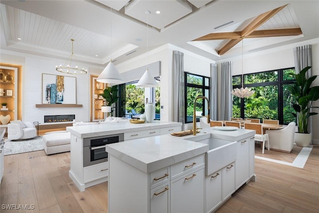 kitchen with stainless steel oven, white cabinetry, an island with sink, and light hardwood / wood-style flooring