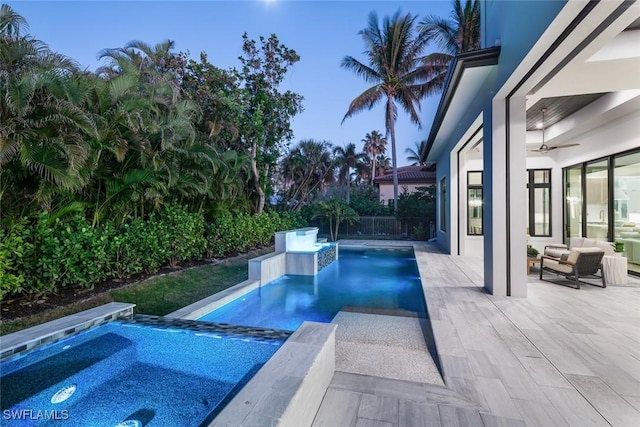 pool at dusk with ceiling fan, a patio area, and an in ground hot tub