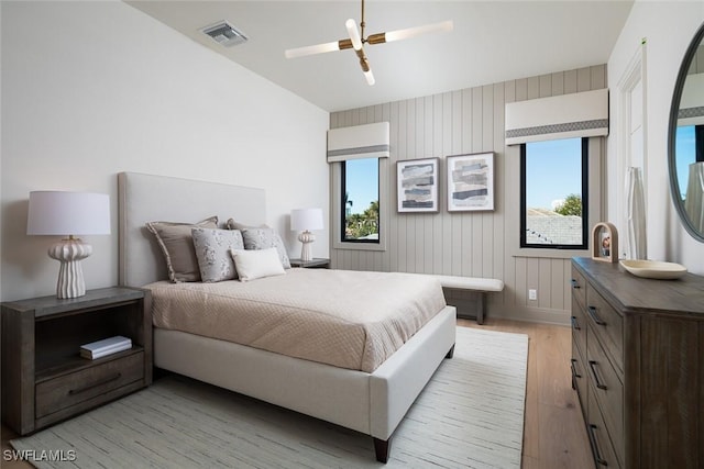 bedroom featuring light hardwood / wood-style floors, multiple windows, wood walls, and ceiling fan