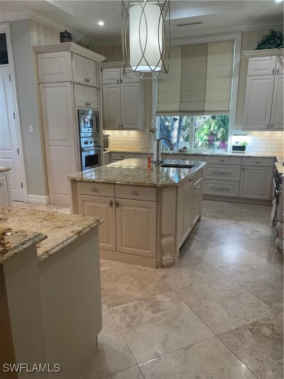 kitchen with decorative light fixtures, sink, light stone counters, stainless steel appliances, and a center island with sink