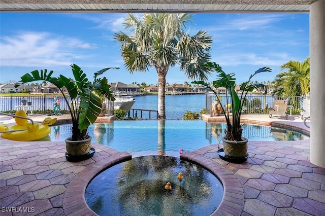 view of pool with a patio area, a water view, and an in ground hot tub