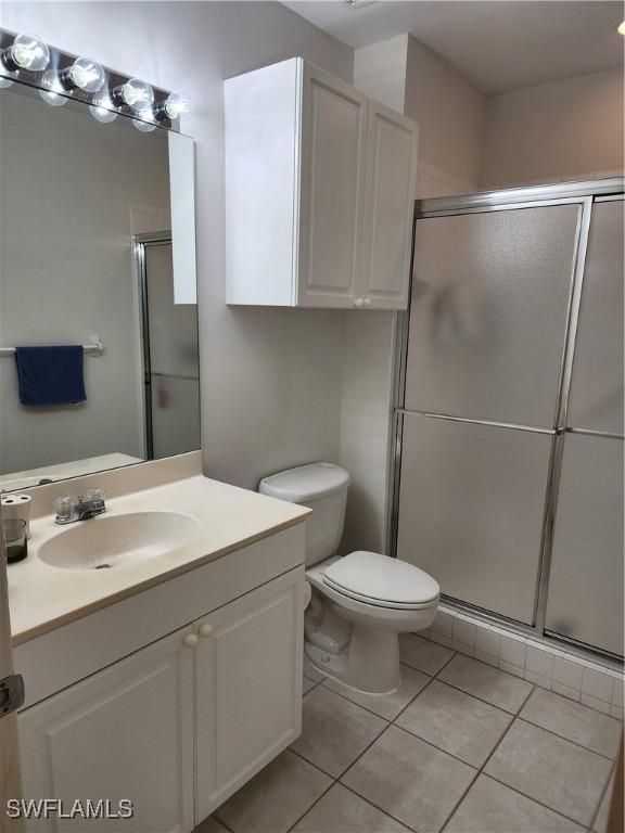 bathroom with tile patterned floors, a shower with door, vanity, and toilet