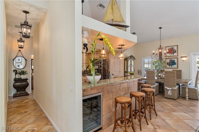 bar with light stone countertops, pendant lighting, wine cooler, and a notable chandelier