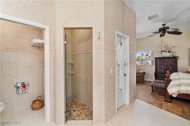 bathroom with ceiling fan, tile patterned flooring, toilet, a shower with door, and tile walls