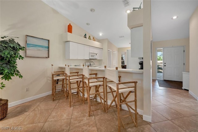 kitchen with high vaulted ceiling, kitchen peninsula, light tile patterned floors, a kitchen bar, and white cabinetry