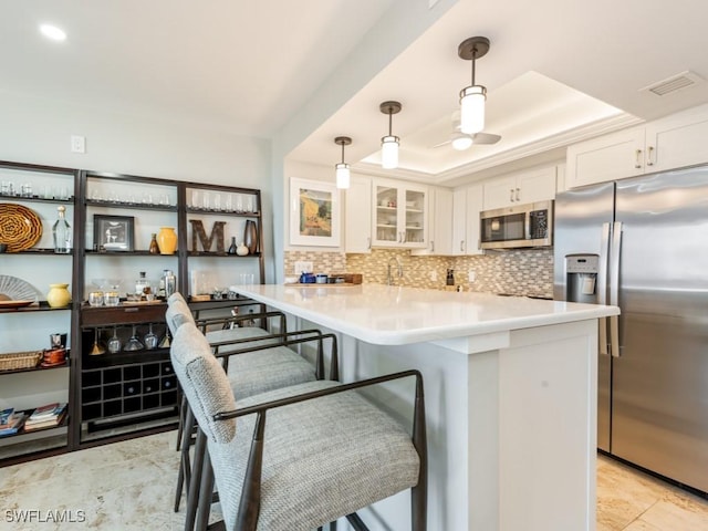 kitchen with white cabinetry, hanging light fixtures, a raised ceiling, a breakfast bar area, and appliances with stainless steel finishes