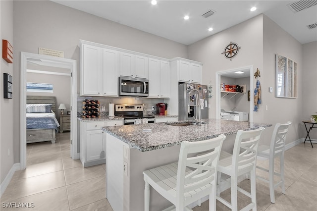 kitchen with stainless steel appliances, a kitchen breakfast bar, independent washer and dryer, a kitchen island with sink, and white cabinets