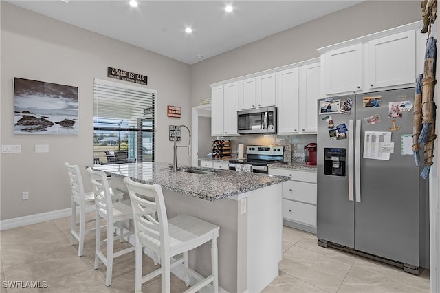 kitchen featuring white cabinetry, sink, stainless steel appliances, light stone counters, and a center island with sink