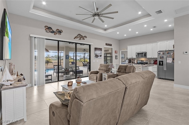 living room with a raised ceiling, ceiling fan, and light tile patterned flooring