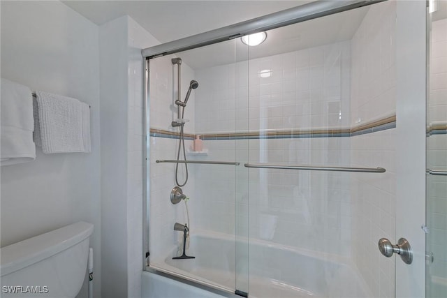 bathroom featuring toilet and shower / bath combination with glass door