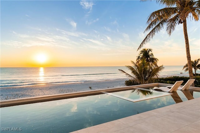 pool at dusk featuring a water view, a jacuzzi, and a view of the beach