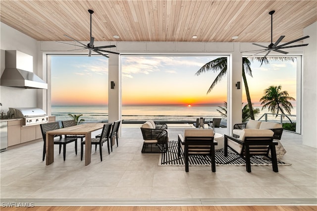 patio terrace at dusk with ceiling fan, an outdoor kitchen, an outdoor hangout area, grilling area, and a water view