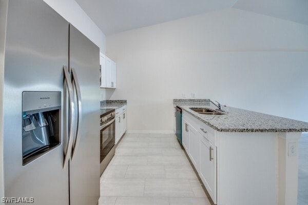 kitchen with lofted ceiling, light stone countertops, white cabinetry, and appliances with stainless steel finishes