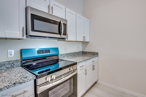 kitchen with white cabinetry, light stone counters, and appliances with stainless steel finishes