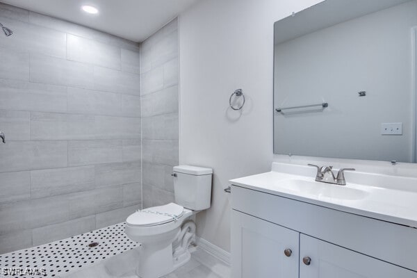 bathroom with a tile shower, vanity, and toilet