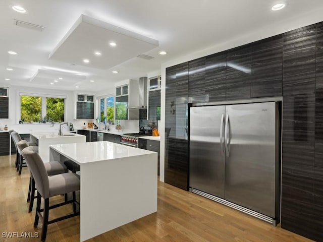 kitchen with a kitchen bar, stainless steel appliances, wall chimney range hood, light hardwood / wood-style floors, and a kitchen island