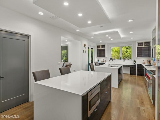 kitchen featuring sink, stainless steel microwave, light hardwood / wood-style flooring, an island with sink, and a breakfast bar