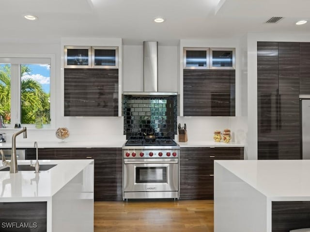 kitchen with sink, wall chimney exhaust hood, designer range, decorative backsplash, and dark brown cabinetry