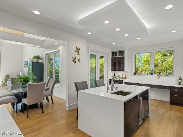 kitchen featuring dark brown cabinets, light wood-type flooring, a center island with sink, and sink