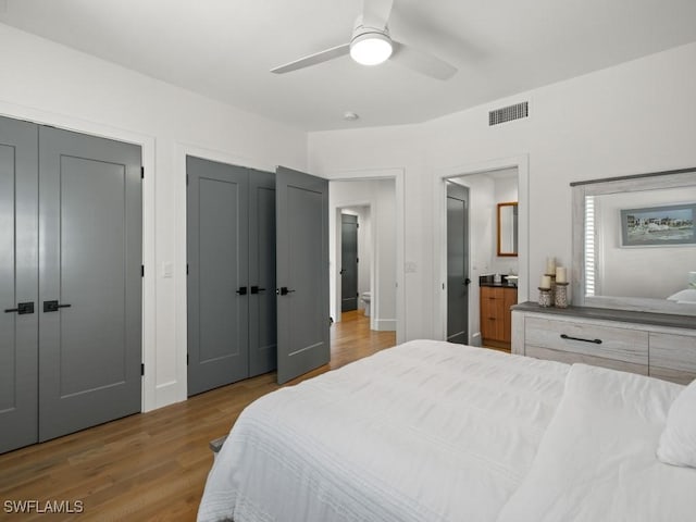 bedroom with multiple closets, ensuite bathroom, ceiling fan, and light hardwood / wood-style floors