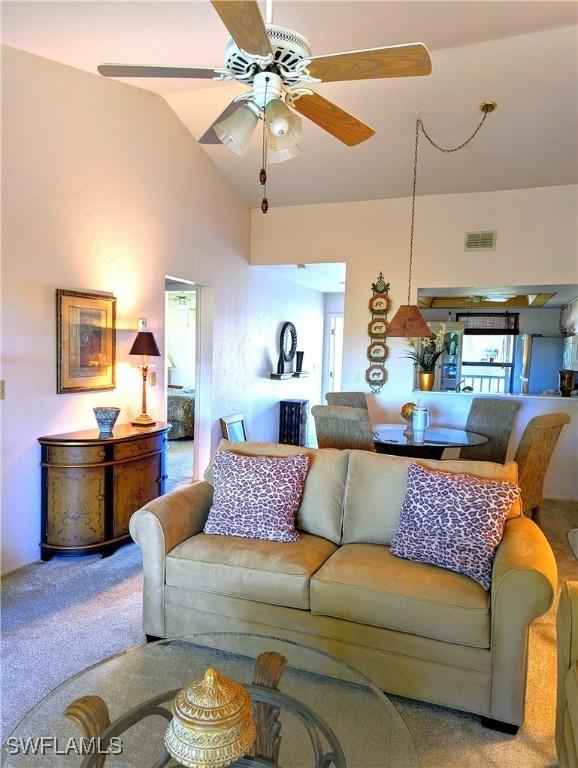 carpeted living room with lofted ceiling, visible vents, and a ceiling fan