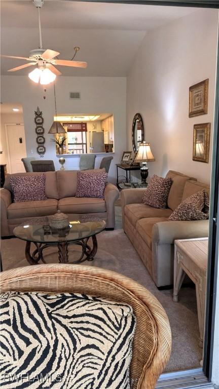 carpeted living room with vaulted ceiling, ceiling fan, and visible vents