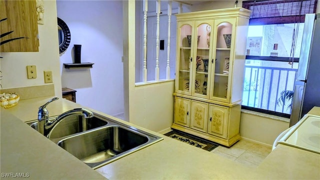 kitchen featuring a sink, tile patterned floors, baseboards, range, and freestanding refrigerator